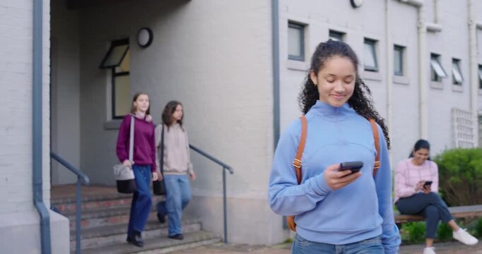 Diverse students exiting brick building, female youth wearing blue top walking to class using phone