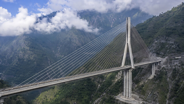 Anji Khad railway cable-stayed bridge crossing a deep Himalayan valley in Jammu and Kashmir, tall single bridge pylon with elegant steel cables, rugged green mountains and drifting clouds