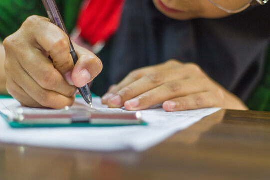 Close up hand filling out a form or exam with pen, paper grid document on desk. Student or employee writing, survey or test paperwork concept.