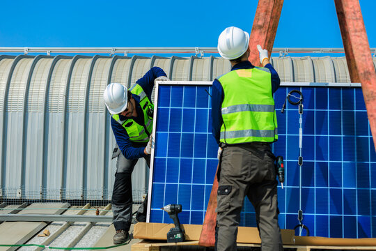 solar energy renewable net zero carbon neutral carbon reduction climate action.Technicians align photovoltaic panels during rooftop solar installation,ensuring safe lifting clean energy production.