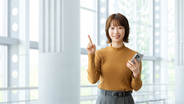 スマートフォンを持って案内をする笑顔の女性・ビジネスウーマン, Smiling Businesswoman Providing Guidance with a Smartphone