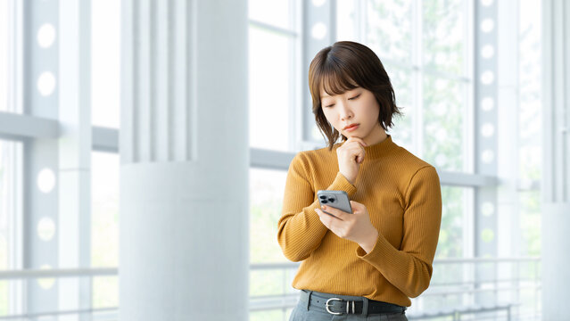スマートフォンを使って考える女性・ビジネスウーマン, Businesswoman Thinking While Using a Smartphone