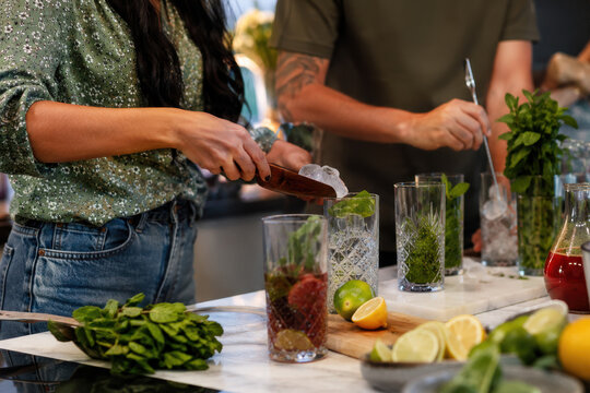 Friends preparing colorful alcohol free cocktails with fresh herbs and citrus. Perfect for wellness campaigns, beverage ads, blogs