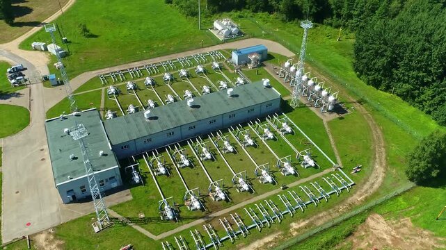 Latvia - 09 October 2023: Aerial view of a natural gas compressor station featuring industrial piping, valves, and equipment situated in a green rural landscape.