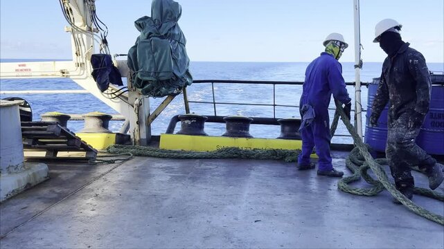 Ship crew uncoiling mooring ropes from winch drums at open sea. vessel aft mooring station.