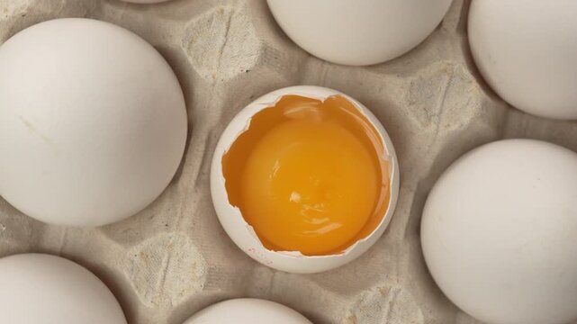 Close-up of raw chicken organic eggs in egg cardboard box. One egg cracked showing the yolk.