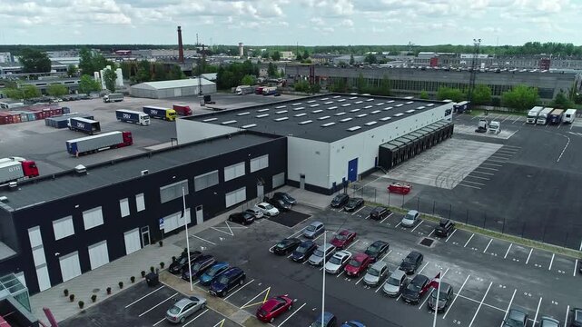 Latvia - 19 February 2023: Aerial view of a large logistics warehouse facility with loading docks, parked trucks, and a parking lot with cars.