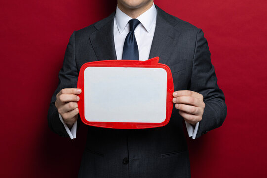 Businessman holding a blank whiteboard with copy space on red background