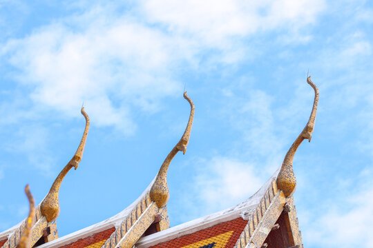 Golden chofah finials crown a traditional Thai Buddhist temple beneath a brilliant blue sky, celebrating timeless craftsmanship, cultural heritage, spiritual architecture and iconic Thailand travel.
