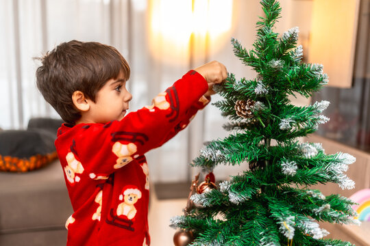 Little boy decorating christmas tree wearing pajamas