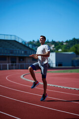 Fototapeta premium Smiling male runner warming up with high knees on outdoor track