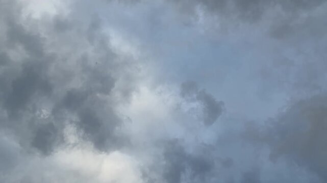 Dark gray clouds drift across an overcast sky, creating a dramatic atmospheric scene with changing light and natural cloud movement before possible rainfall. Wide shot.