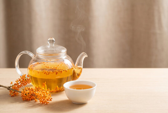 Japanese osmanthus kinmokusei herbal tea in glass teapot with orange autumn blossoms and copy space