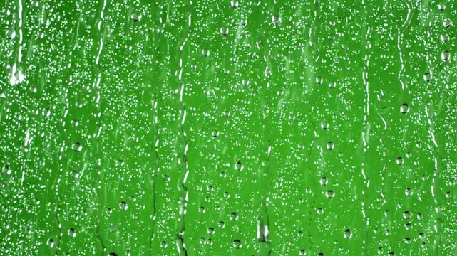 Rain drops fall on window glass in a bright colored setting during a rainfall event