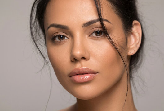 A striking close-up portrait of a young woman with dark hair styled in a loose updo, featuring wispy strands framing her face