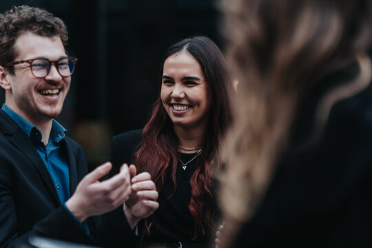Young professionals laughing and networking during an informal business conversation. Colleagues share a light moment while socializing outdoors.