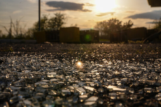 Broken glass pieces glimmer on a dirt road against a sunset backdrop. Concept of environmental impact, fragility, contrast of nature and human activity, ideal for editorial use.