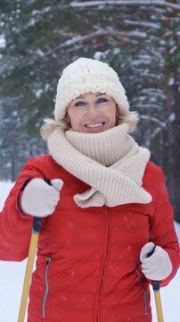 Cheerful senior woman engaging in a nordic walk through a picturesque winter park, smiling contentedly as snowflakes gently fall around her, embodying a healthy and active lifestyle