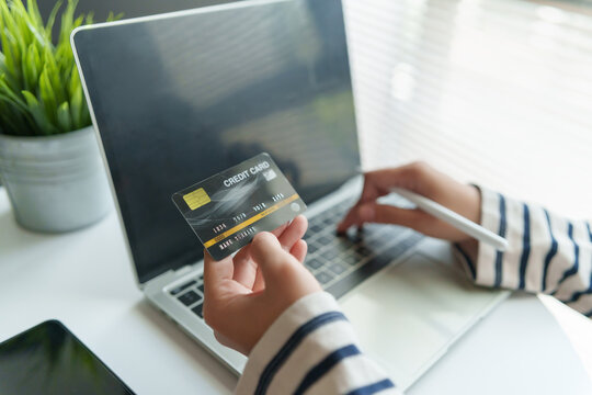 Woman holding a credit card while shopping online with a laptop at home, representing secure digital payment, e-commerce and modern consumer lifestyle.
