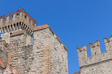 Rough stone walls and brick-tipped battlements rise in a close upward view of Scaligero Castle in Sirmione, northern Italy. © Artem
