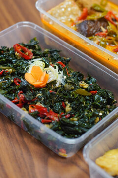 Close up of oseng daun singkong, Indonesian stir fried cassava leaves with chili and spices, served in plastic container, traditional vegan Asian vegetable dish
