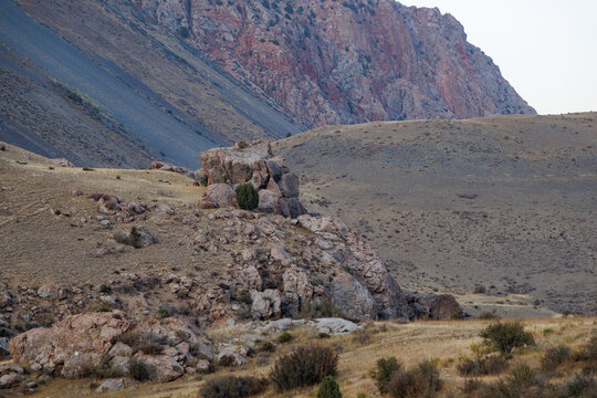 Unique rock formation on a grassy hill with layered mountain slopes in Fann Mountains, Tajikistan