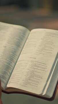 Hand turning pages of open Spanish Holy Bible in sunlight