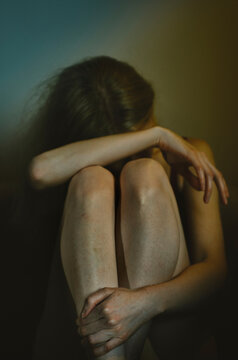 Vulnerable unrecognizable woman sitting in a dark room hiding face