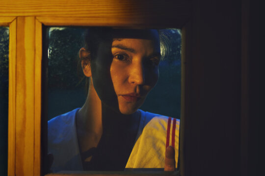 Woman looking through a glass window at night with dark shadow