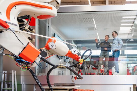 Male engineers observe an industrial robot from an office cube