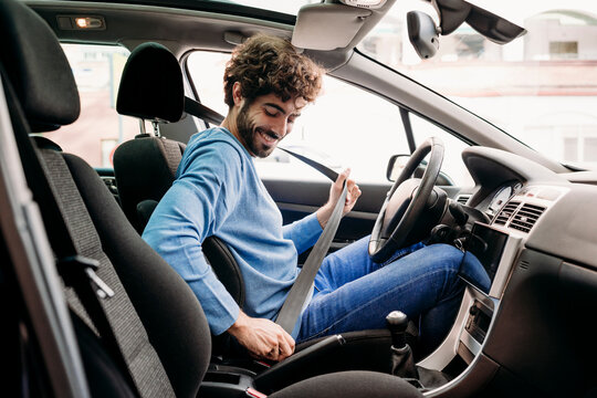 Young man fastening seat belt sitting in car