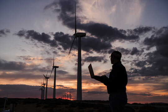 Silhouette of engineer working on laptop at wind farm