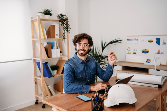 Thoughtful young engineer with laptop on desk in office