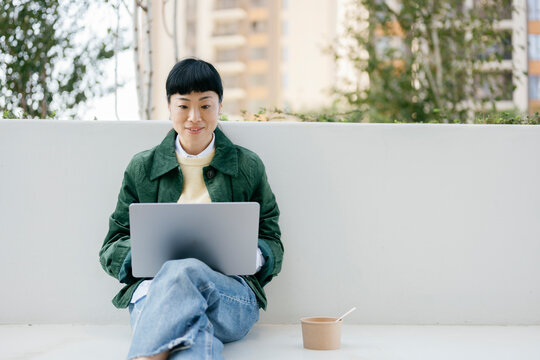 Woman sitting outdoors in urban setting using laptop during lunch break
