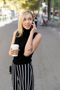 Portrait of smiling blond woman with coffee to go on the phone