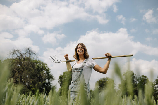 Young woman with hay fork standing in a grain field in the countryside
