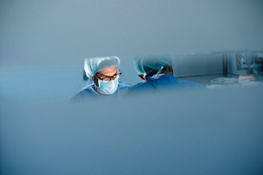 Male surgeons seen from glass while performing operation in hospital