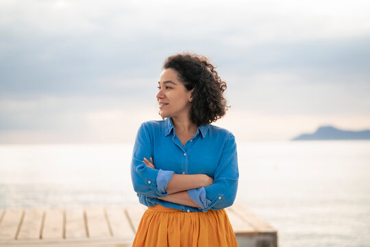Contemplative woman with arms crossed standing in front of sea