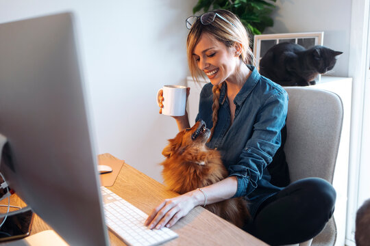 Smiling female influencer looking at dog while having coffee at home
