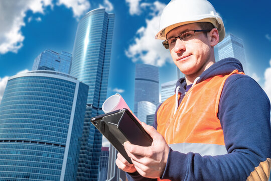 Urban construction. Engineer checks project documentation with tablet near modern skyscrapers and commercial business district