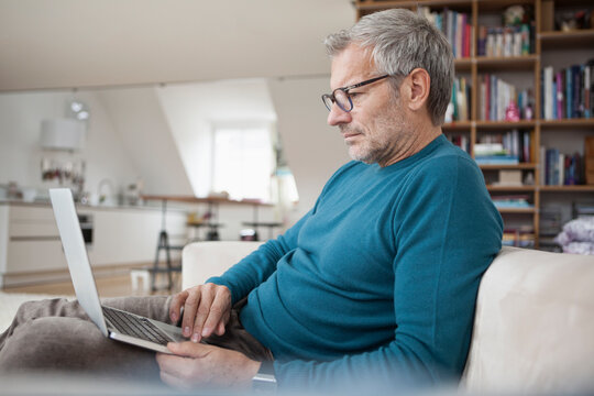 Mature man at home sitting on couch using laptop