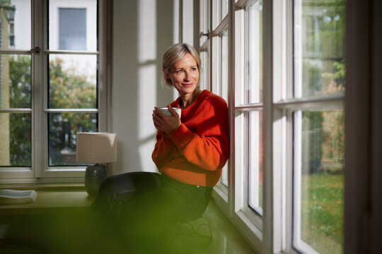 Smiling woman holds a warm cup by the window in a peaceful home