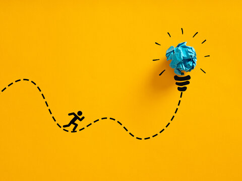 Person running an erratic path towards a crumpled paper lightbulb idea. Pursuing creative ideas.