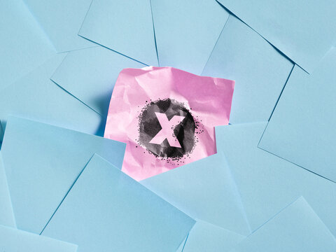 Crumpled pink note with X marking standing out symbolizing error, rejection, mistake or cancellation.