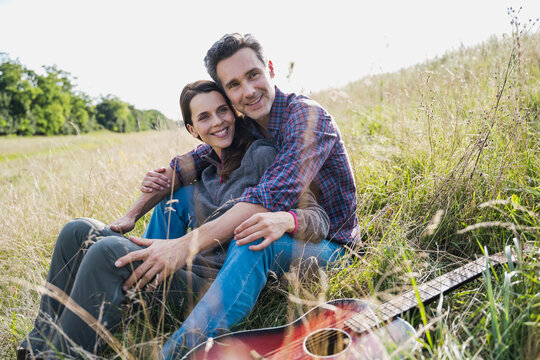 Smiling couple embracing in a grassy field with a guitar outdoors