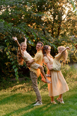 Fototapeta premium A happy family is playing outdoors in the park in summer. Dad, mom, and two daughters are hugging and laughing