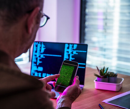 Man uses smartphone for coding and cybersecurity at office desk