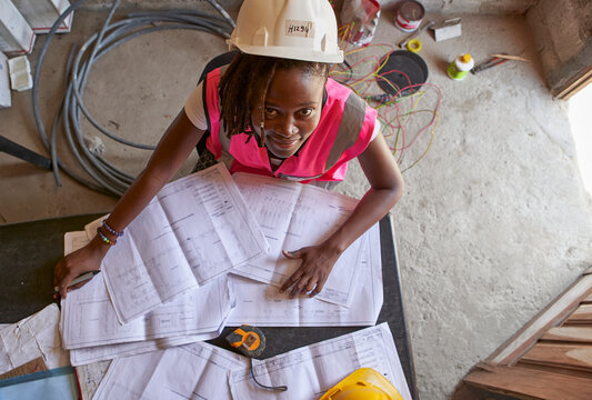 Smiling building contractor with blueprints on desk sitting in school at site