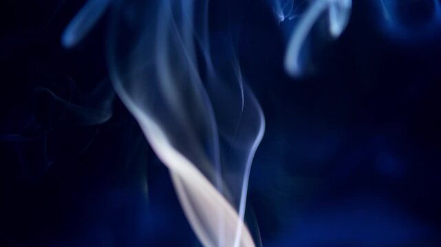 Abstract blue smoke rising and swirling on a dark background creates an ethereal and mysterious atmosphere, a slow motion effect. This fluid motion and nebular texture are creative design elements