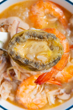 Seafood congee with abalone, prawn and squid held on a ceramic spoon